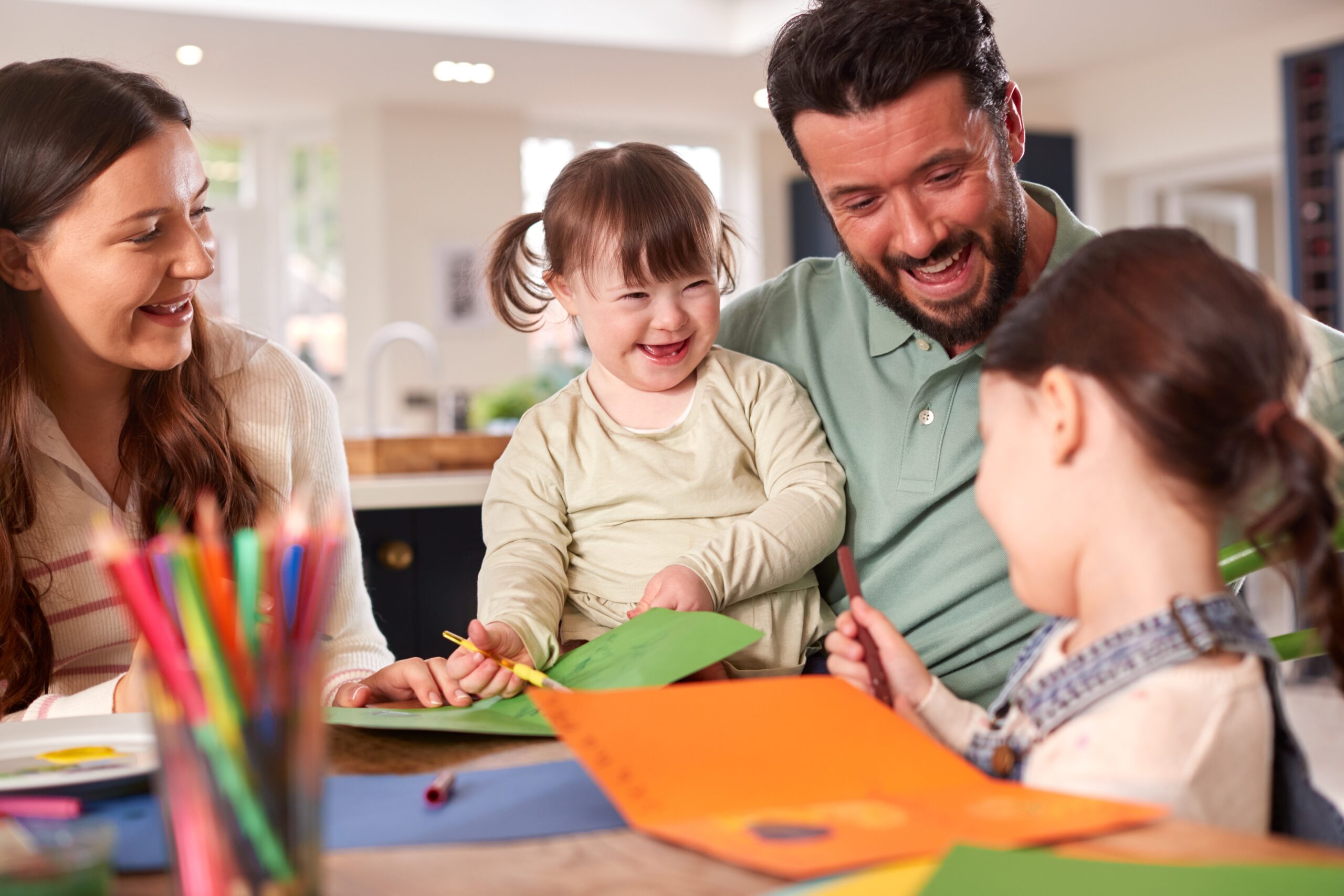 Family,With,Down,Syndrome,Daughter,Sitting,Around,Table,At,Home